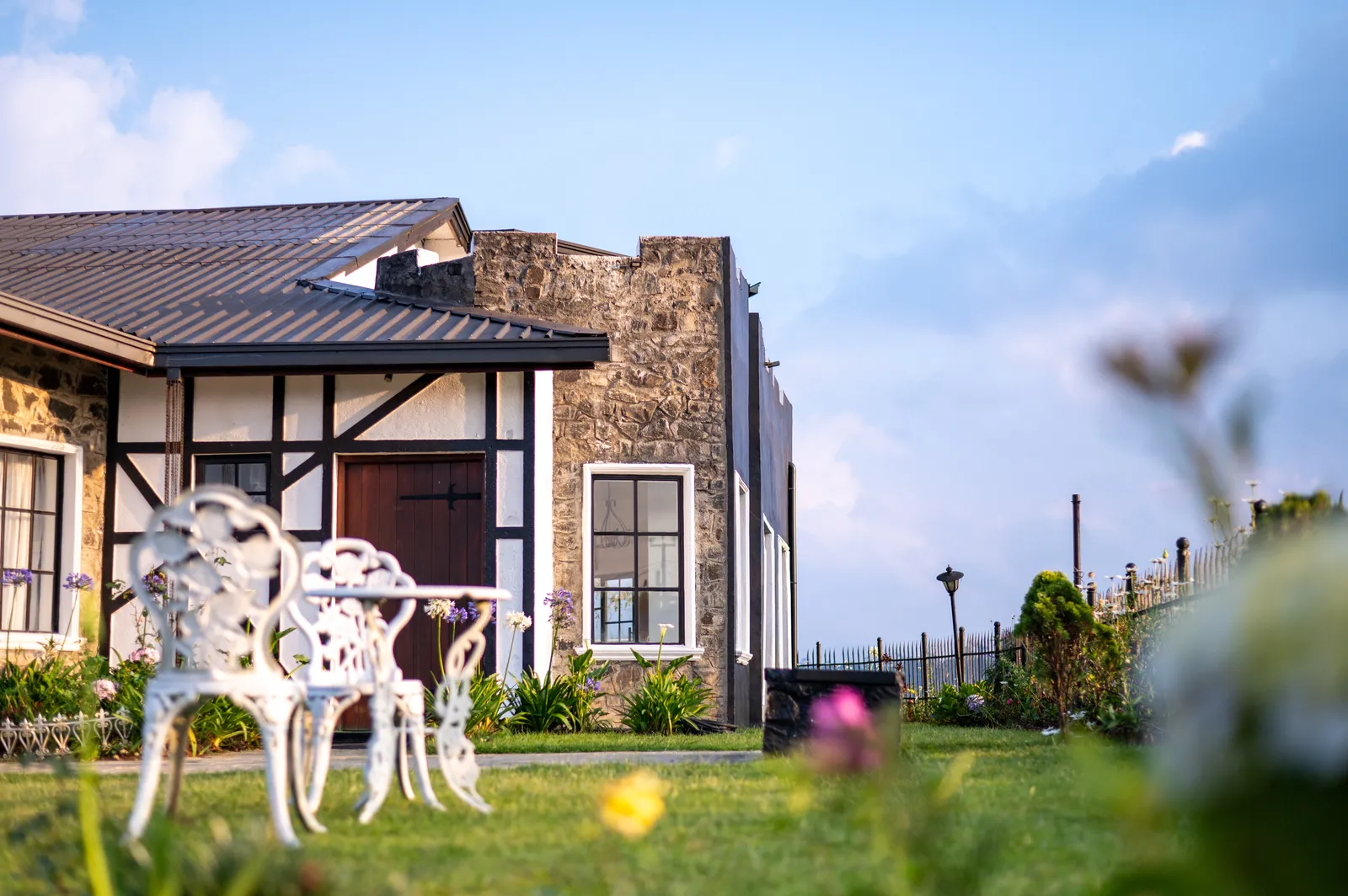 The stone front of Dover Cottage with white iron garden chairs on the lawn