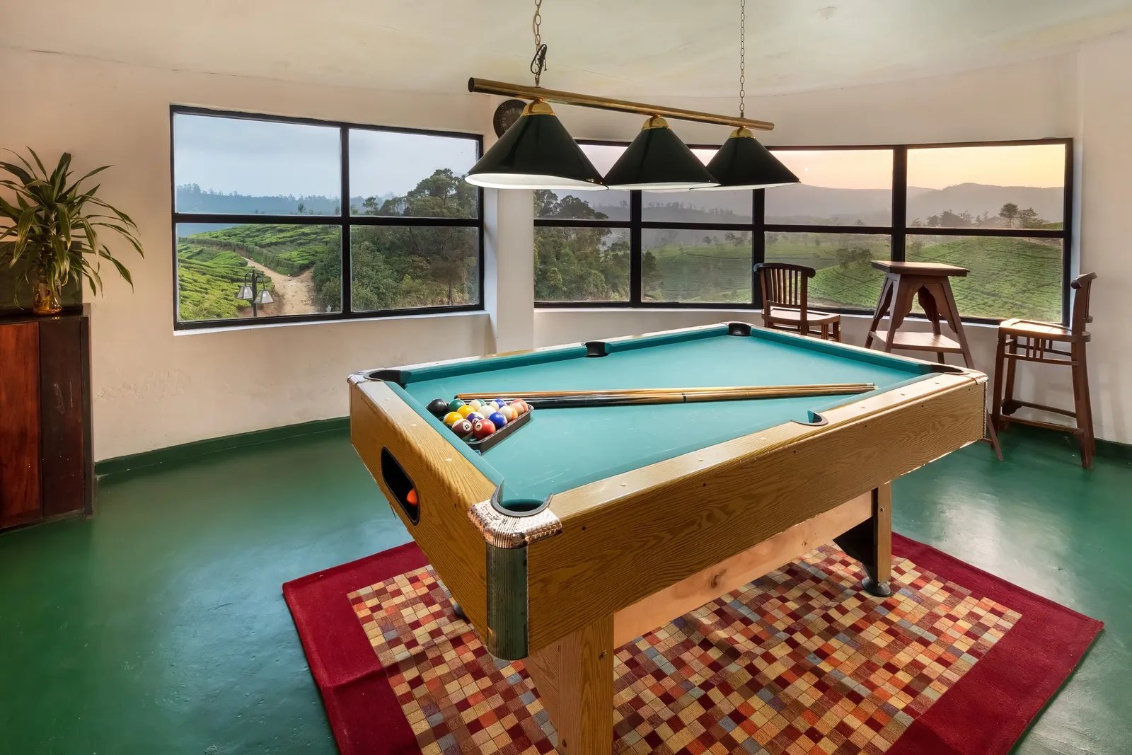 The games room: a pool table under three green lamps, tea fields through the window