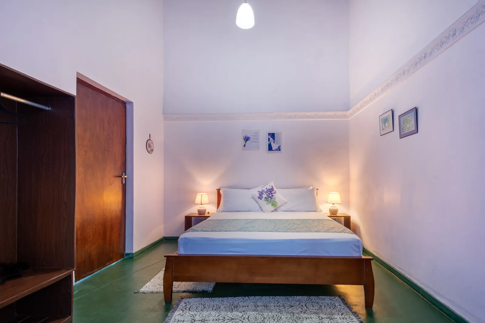 Lavender bedroom: a double bed with a lavender runner, a lamp each side, an open wardrobe and a high white ceiling