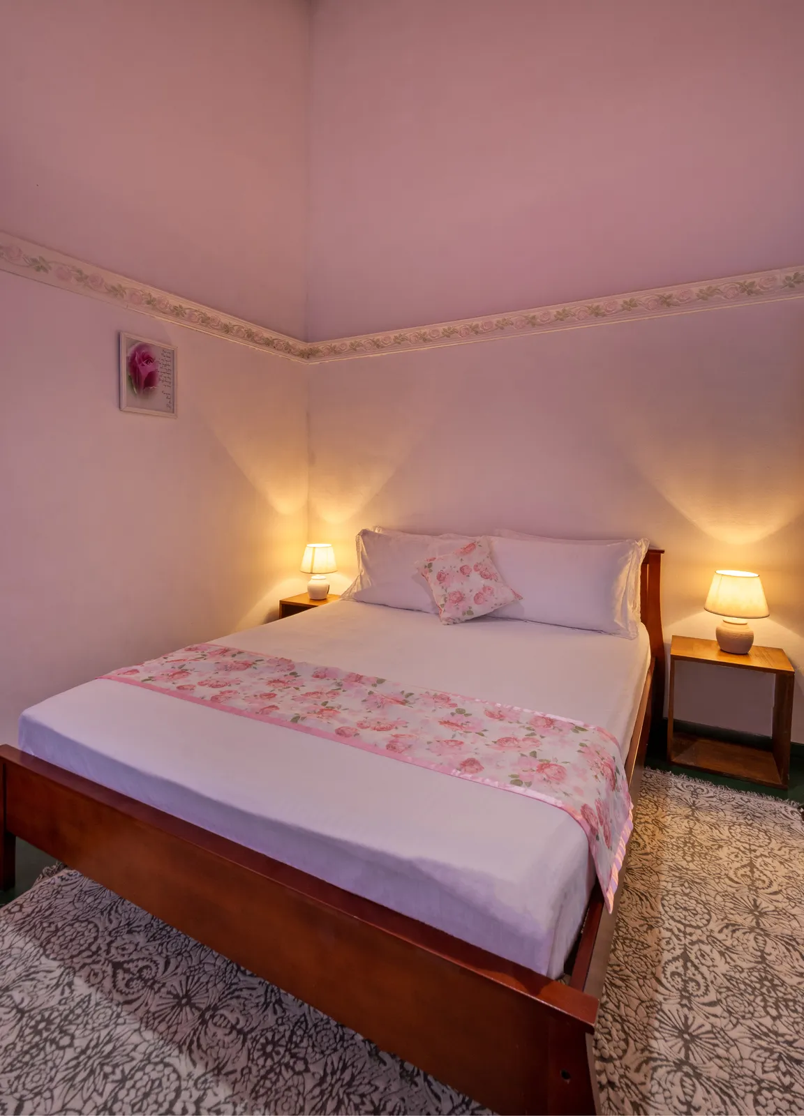 Rose bedroom: a double bed with a pink floral cover, lamps either side and a pink-washed wall
